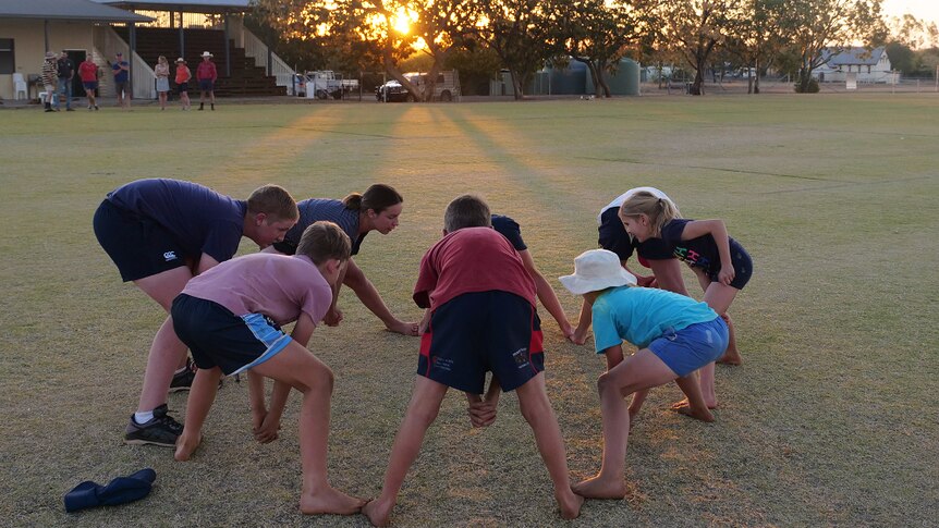 Kids stand in a circle playing a game as the sun sets through a tree in the background
