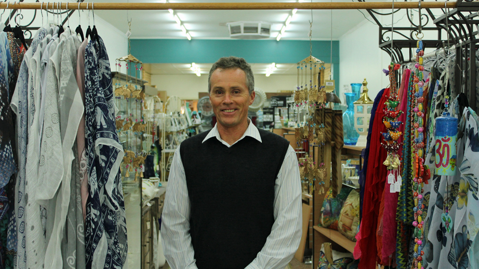 A man in a white shirt and black vest standing in a store surrounded by giftware.