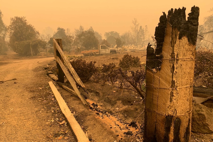 The burnt-out remains of a fence destroyed by fire, as a thick yellow haze hangs over.