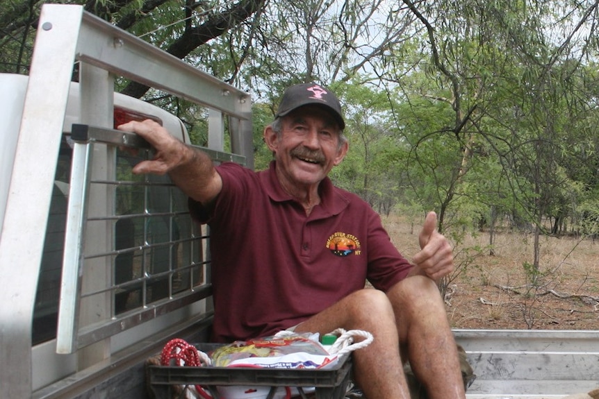 Man Paddy Moriarty sitting in the tray of a utility vehicle smiling and giving a thumbs-up