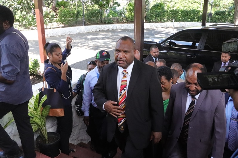 James Marape walks up some steps with a crowd of people behind him.