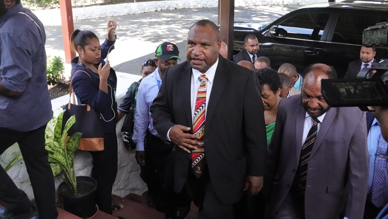 James Marape walks up some steps with a crowd of people behind him.