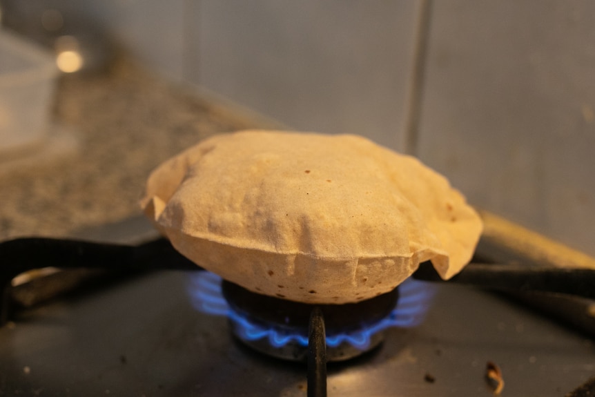 An Indian bread puffs up on a flame of a gas stove.