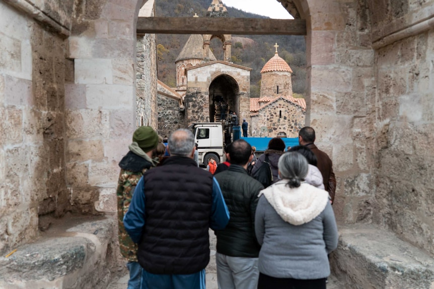 The backs of people lining up to walk through a brick arch