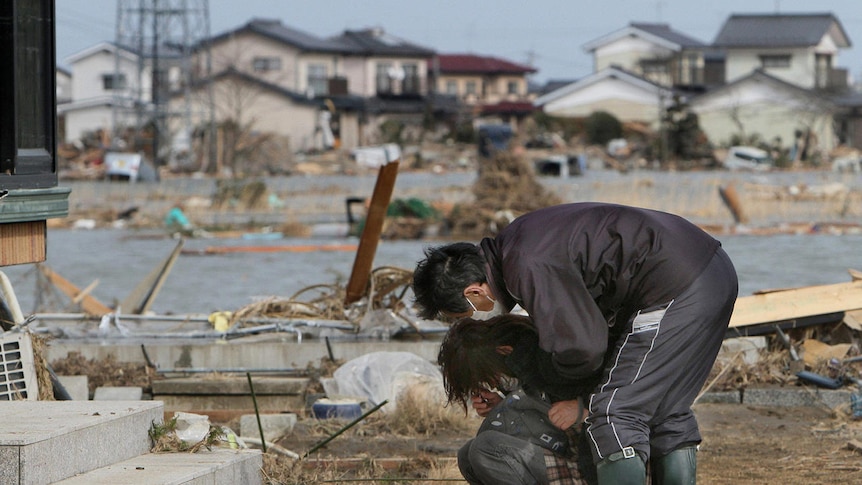 A woman cries in front of her damaged home in the town of Watari