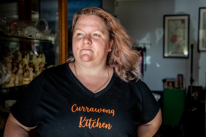 Chandelle porte un t-shirt noir imprimé des mots « Currawong Kitchen » et regarde pensivement au loin.