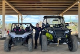 A young girl stands between two four-wheeled buggies which she uses to compete.