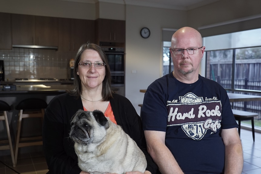 Sam and Wayne sitting together in their home, with a pug dog sitting on Sam's lap.