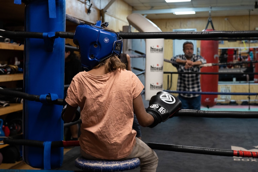 A young person sitting in the corner of a boxing ring.