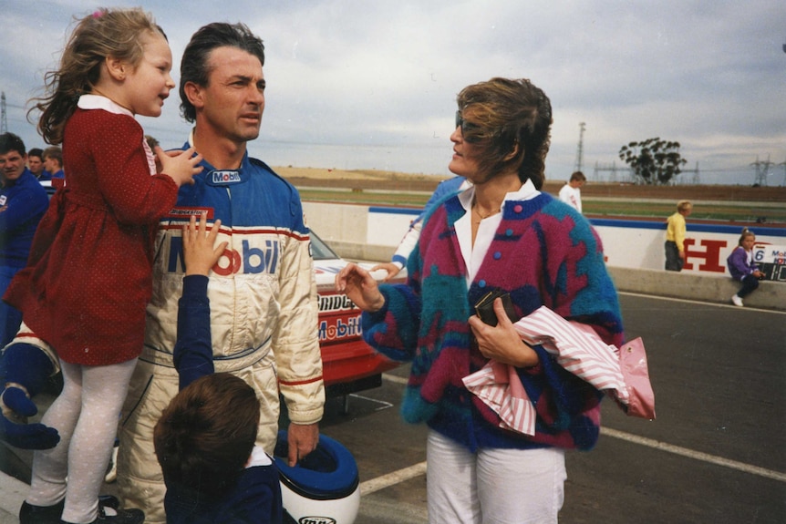 A man talking to a woman holds a girl while a boy reaches up to him.