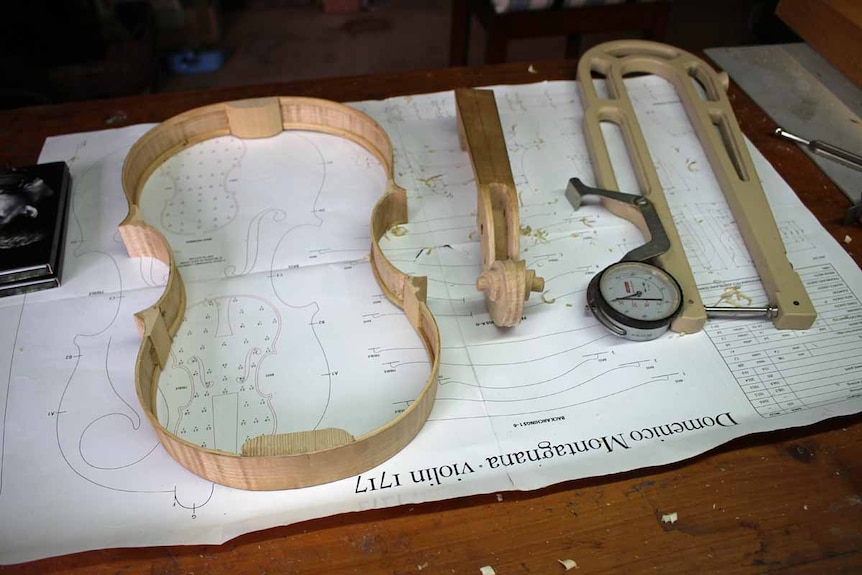 Pieces of a violin lay on a desk next to a measuring instrument.