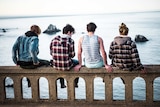 Four men sit along a bridge with their backs facing the camera
