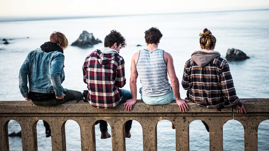 Four men sit along a bridge with their backs facing the camera