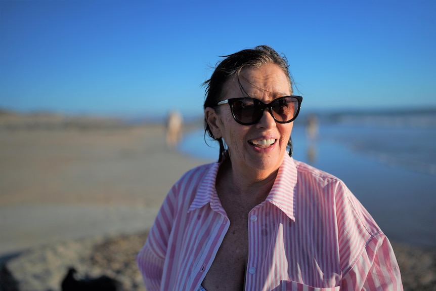 Woman wearring stripe pink and white collared shirt fresh out of the surf wearing sunglasses