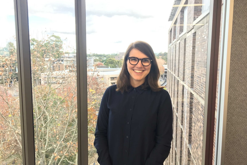 Dr Calabretto stands in front of a window looking out on a leafy university campus.