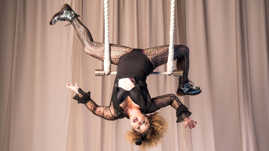 A woman hangs upside down on a trapeze