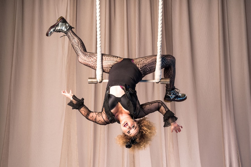 A woman hangs upside down on a trapeze