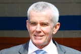 One Nation senator Malcolm Roberts walks in a suit smiling