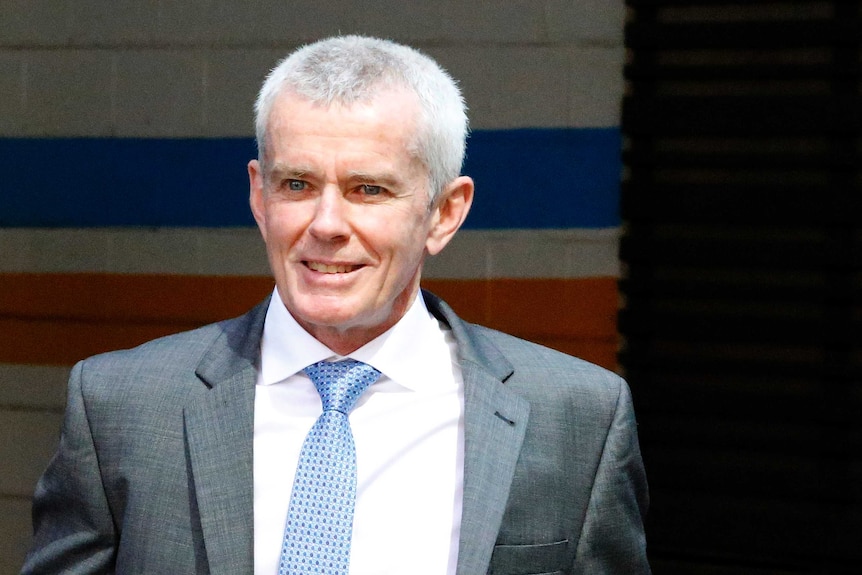 One Nation senator Malcolm Roberts walks in a suit smiling