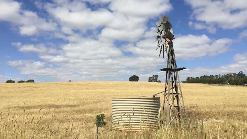 A windmill and a water tank in a dry paddock.
