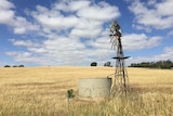 A windmill and a water tank in a dry paddock.