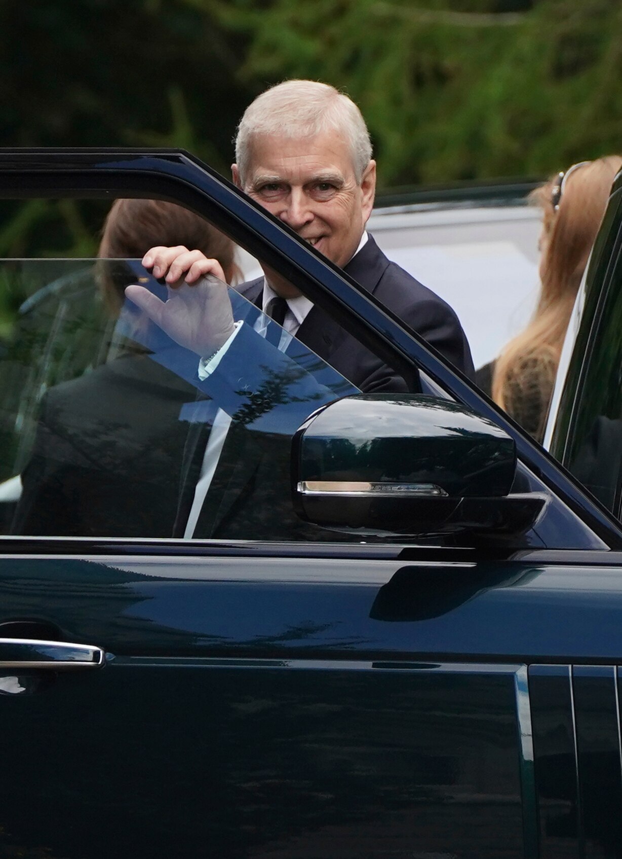Prince Andrew smiles as he gets out of a black car. 