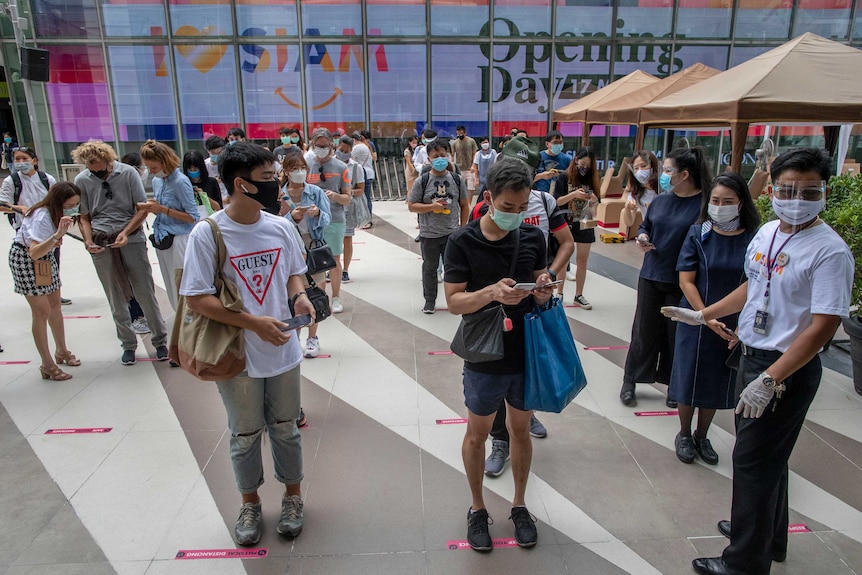 Patrons to an upmarket mall in Bangkok stand whiles maintaining social distance at the entrance.