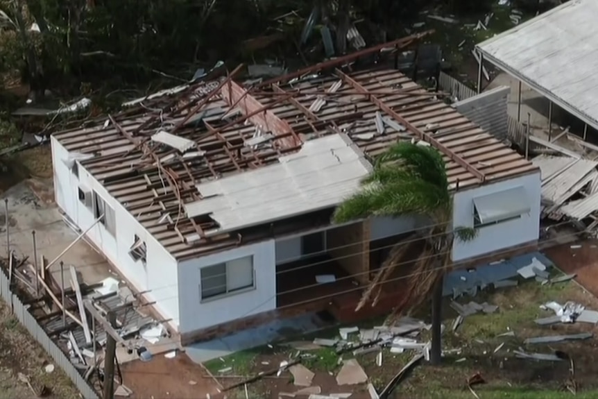 A drone aerial photo of a house with its roof destroyed and debris all around on the ground.