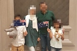 A family of two adults and two children with blurred faces, holding Australian flags and a toy kangaroo and koala
