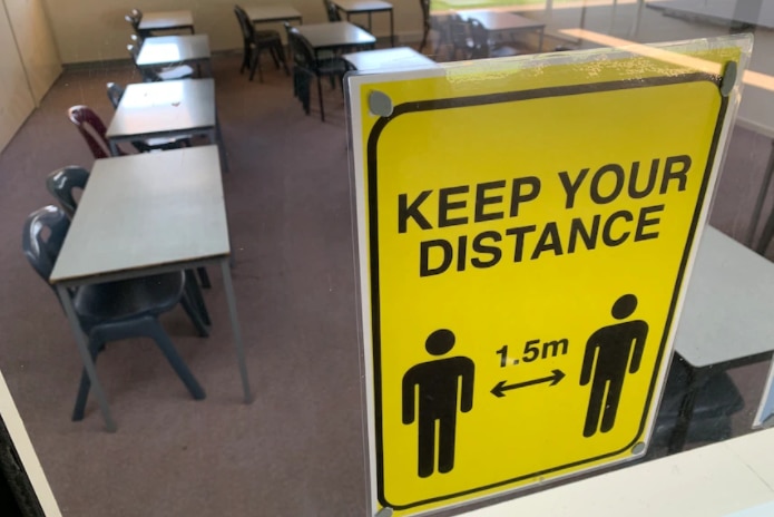 An empty classroom with a yellow board with "KEEP YOUR DISTANCE" on it.