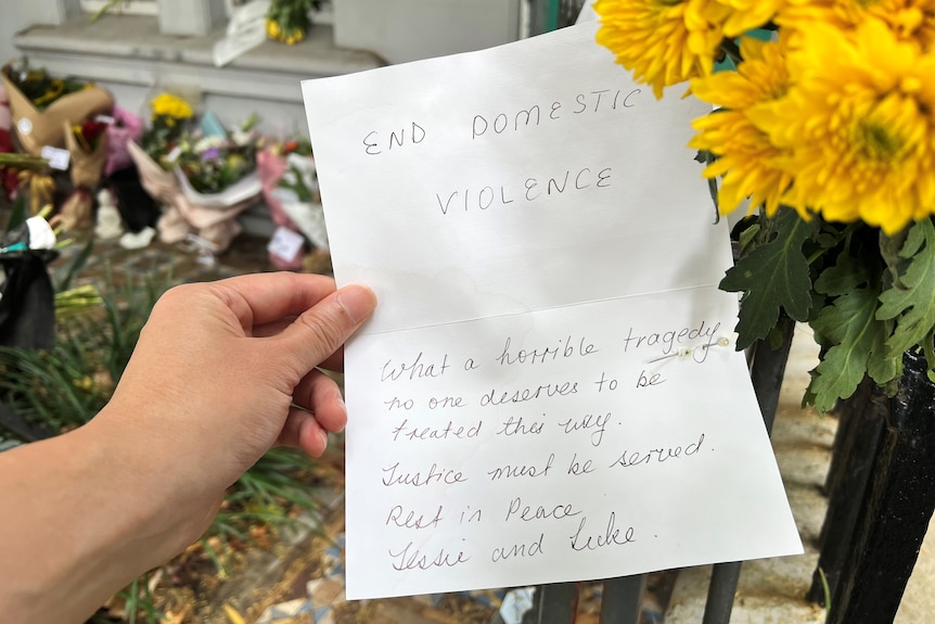 A handwritten note saying 'End domestic violence' outside a terrace home with flowers.