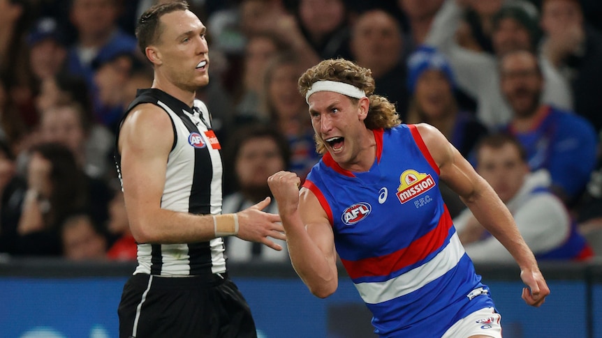 Aaron Naughton clenches his fist while a Collingwood defender looks disappointed behind him