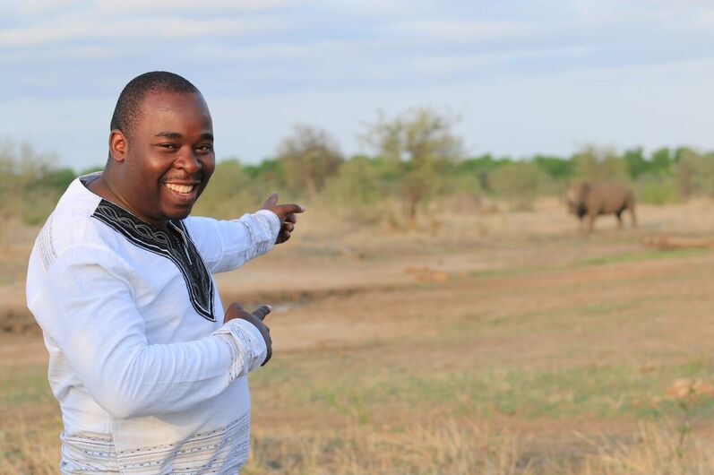 Dingani Masuku smiling and pointing to a rhinoceros at conservation park in Zimbabwe.