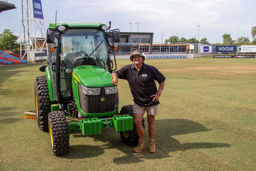 a man standing next to a small tractor on an oval.
