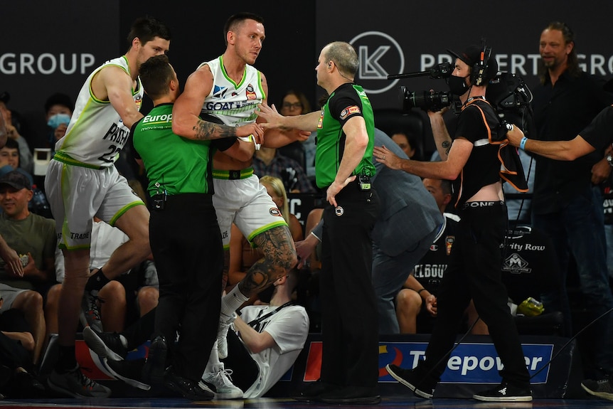  Phoenix's Mitchell Creek being held back by umpires as players scuffle during the NBL match
