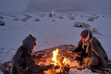 Two people sit in the middle of the snow around a fire in Saudi Arabia