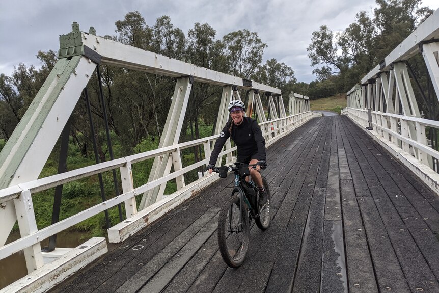 A woman on a bike on an old wooden bridge with white sides.