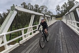 A woman on a bike on an old wooden bridge with white sides.