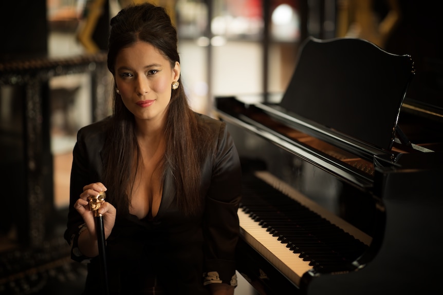 Elle-May sits beside a piano, hand on her cane that has a skull on top.