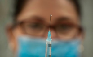 A woman out of focus looking at a syringe.