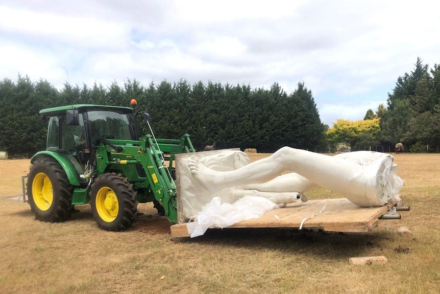 A forklift carries a large statue of a man's legs