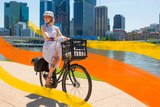ABC radio presenter Katherine Feeney riding her bike along the Brisbane River in a dress and heels
