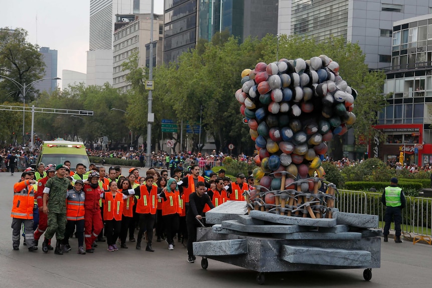 Rescue workers and volunteers march behind a fist made out of safety helmets as they lead the parade.