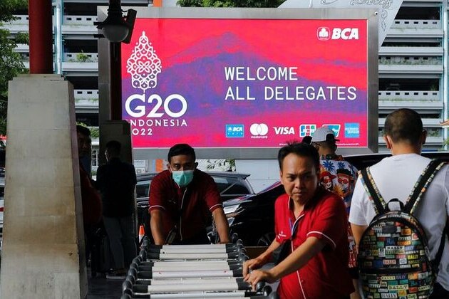 Balinese workers pushing trolley in front of the G20 screen.