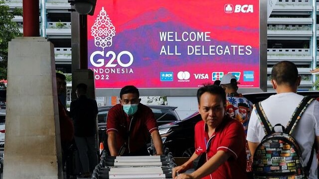 Balinese workers pushing trolley in front of the G20 screen.