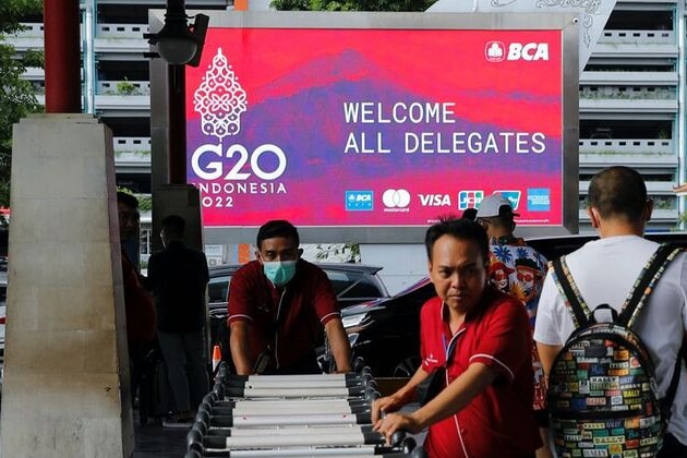 Balinese workers pushing trolley in front of the G20 screen.