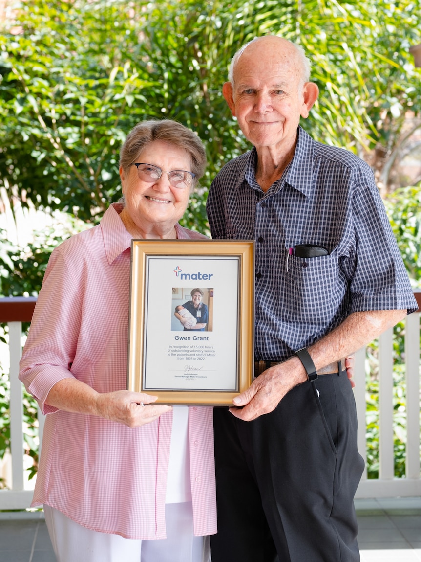 An elderly man and woman holding a framed photo.