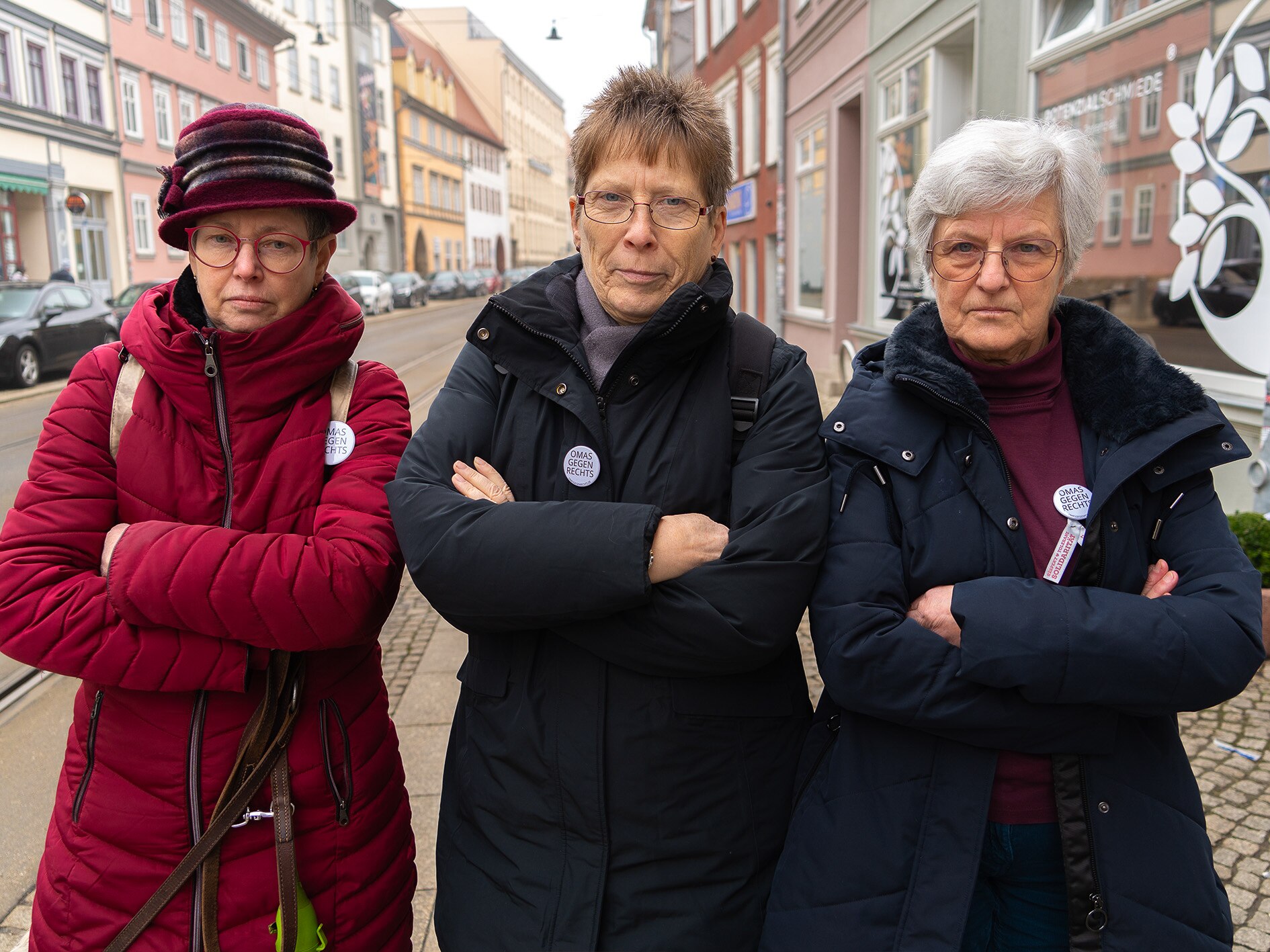 Three women stand with their arms crossed and serious expressions on their faces.