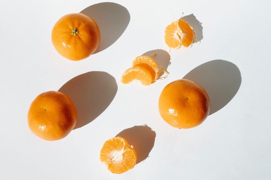 Three whole mandarins and some arranged segments on a blank backdrop.