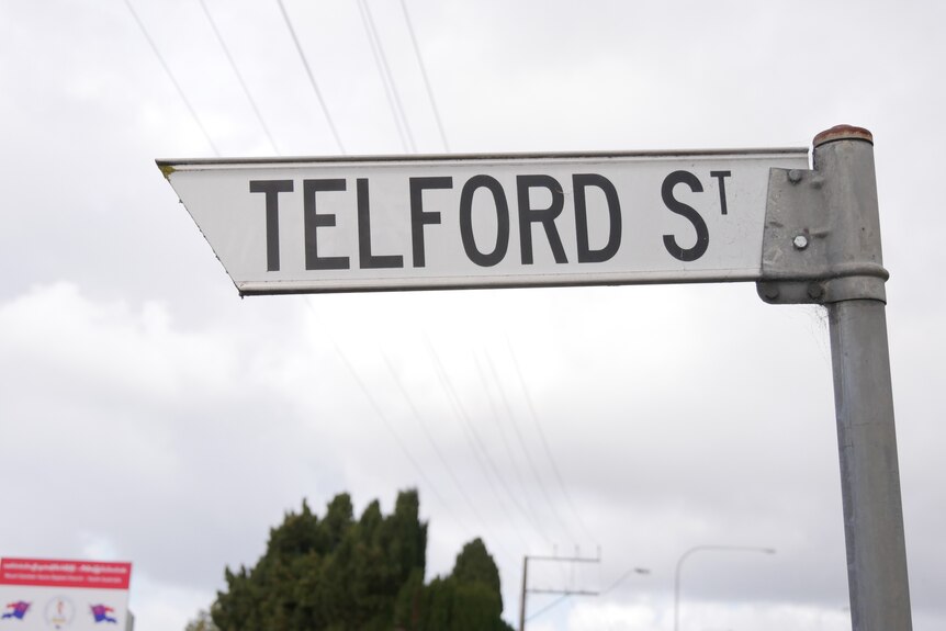 A street sign reading 'Telford St' with a grey sky and powerlines in the background